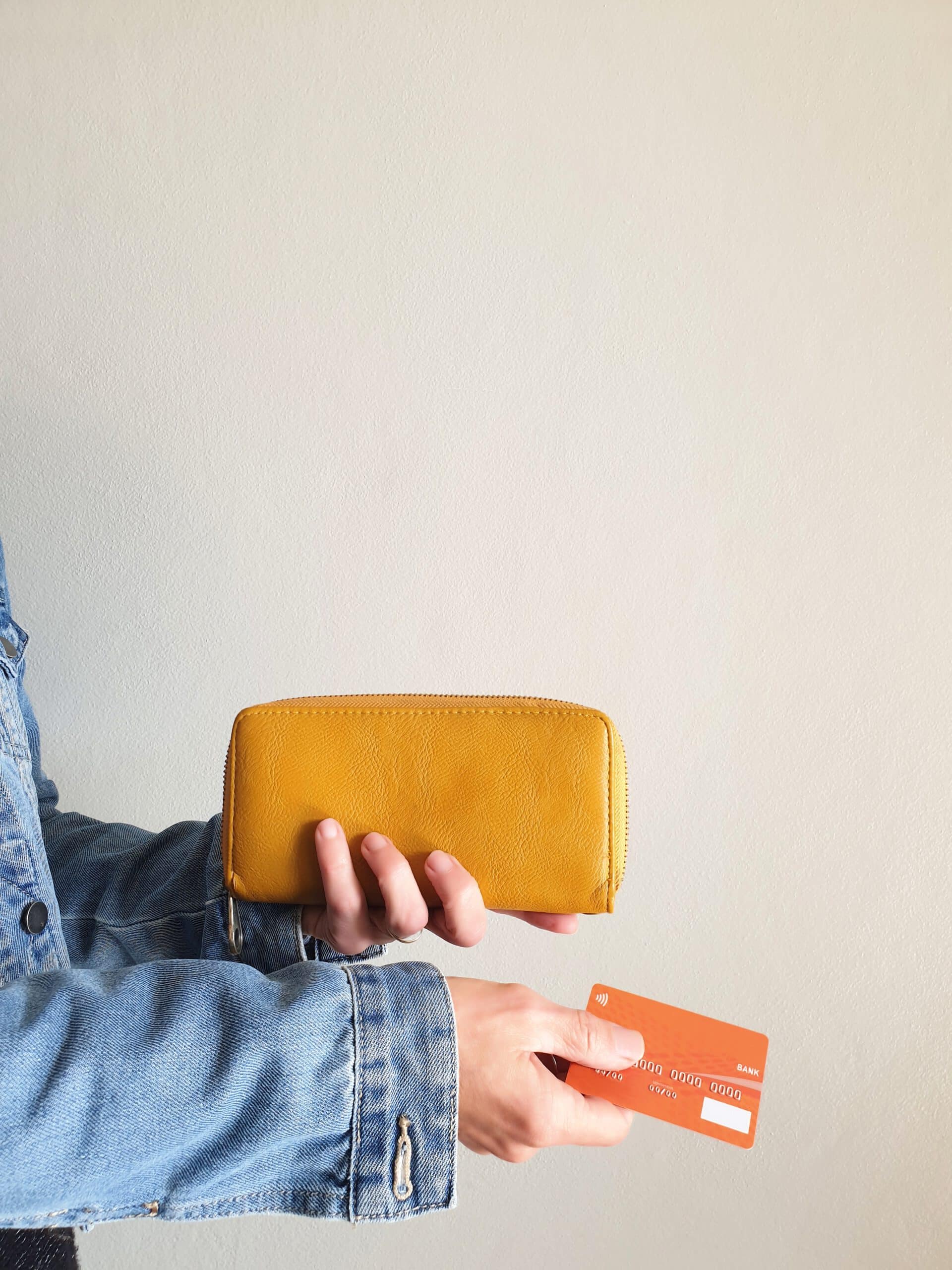 Frau in Jeansjacke hält ihr Portemonnaie und ihre Kreditkarte seitlich in den Händen