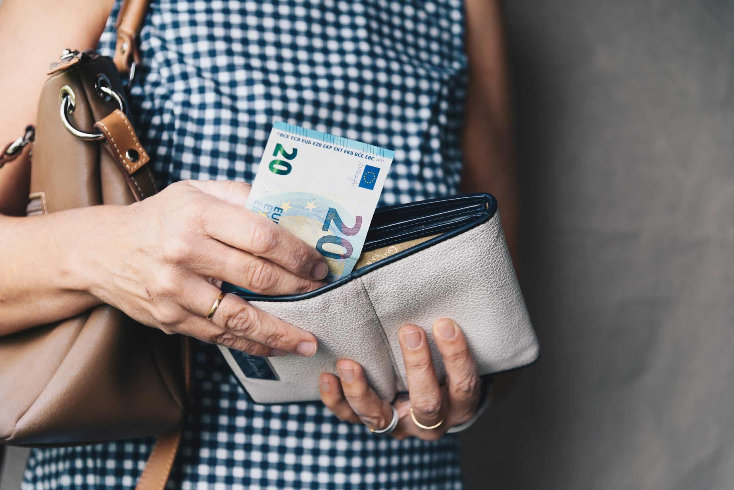 Junge stylische Frau nimmt Geldschein aus ihrem Portemonnaie